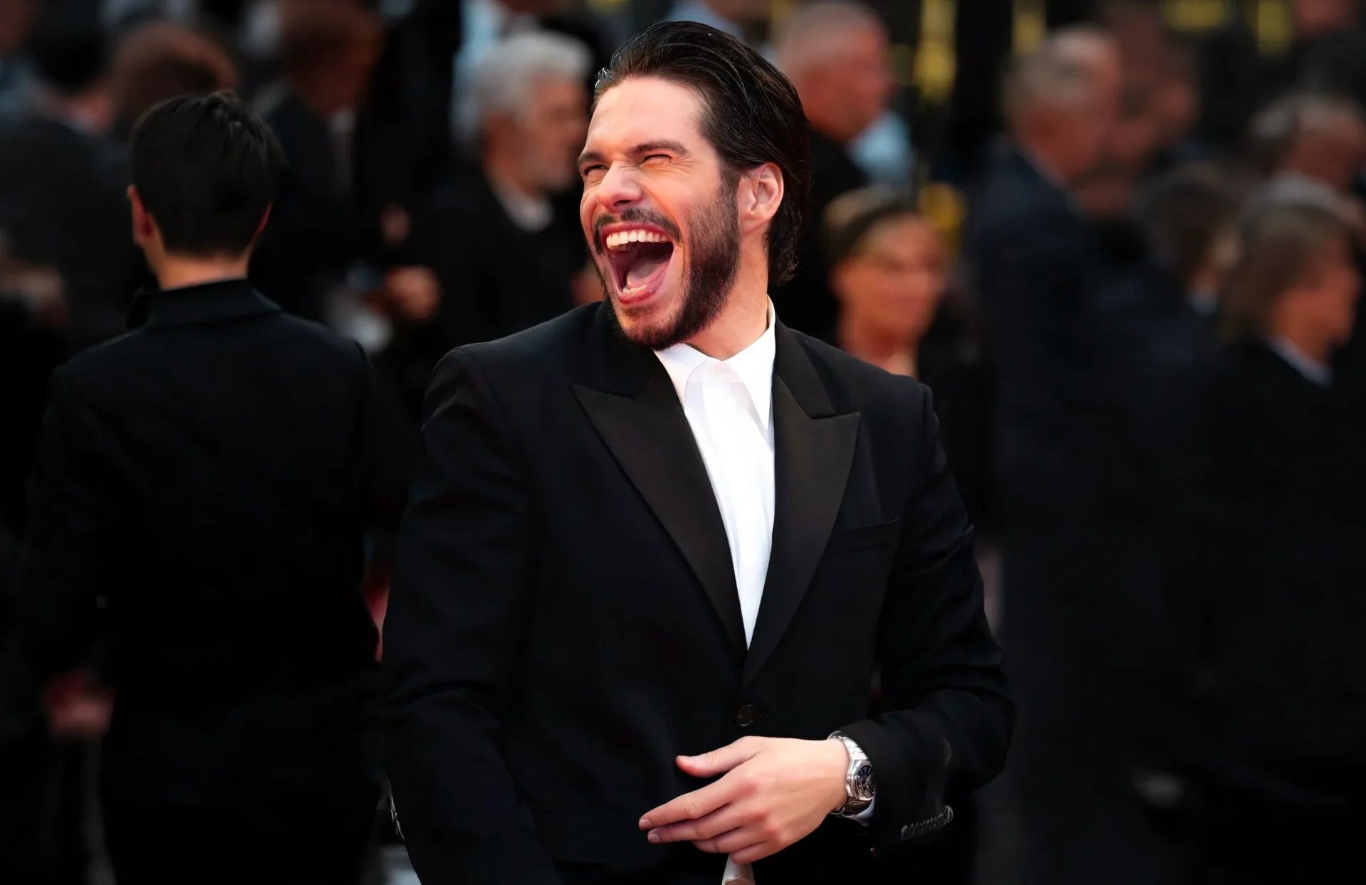 Un homme en smoking noir partageant un éclat de rire sur un tapis rouge
