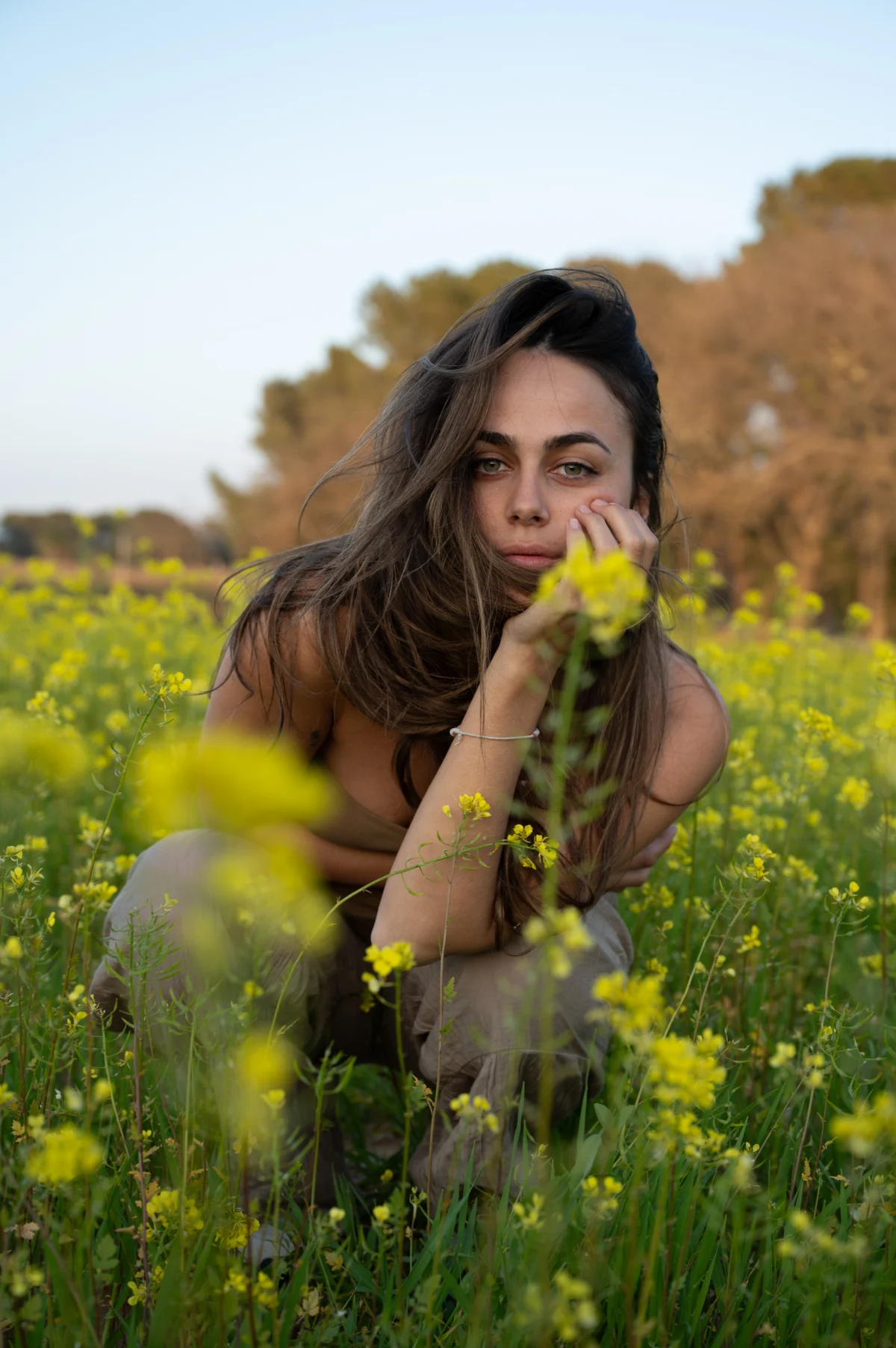 Jeune femme accroupie dans un champ de fleurs jaunes, main sous le menton : photo brute, avant retouche, à Saint-Raphaël