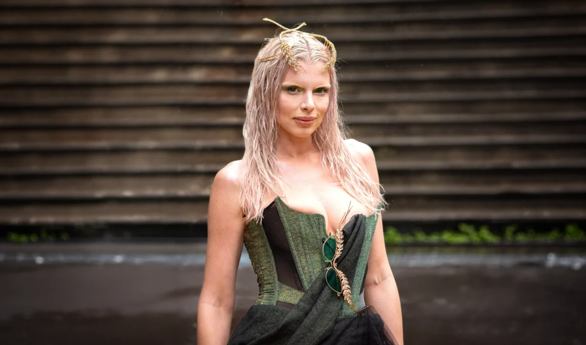 Julia Fox aux cheveux rose pâle effet mouillé, en corset vert et gris, devant des gradins au défilé Vivienne Westwood