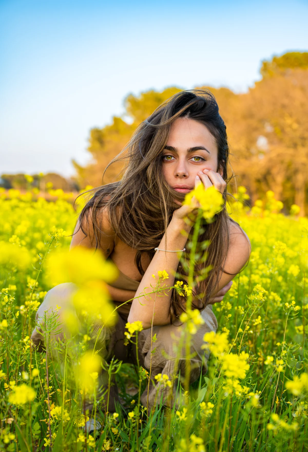 Jeune femme accroupie dans un champ de fleurs jaunes à Saint-Raphaël, main sous le menton : version retouchée